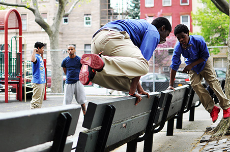 Middle school boys vault over park benches during parkour enrichment class.