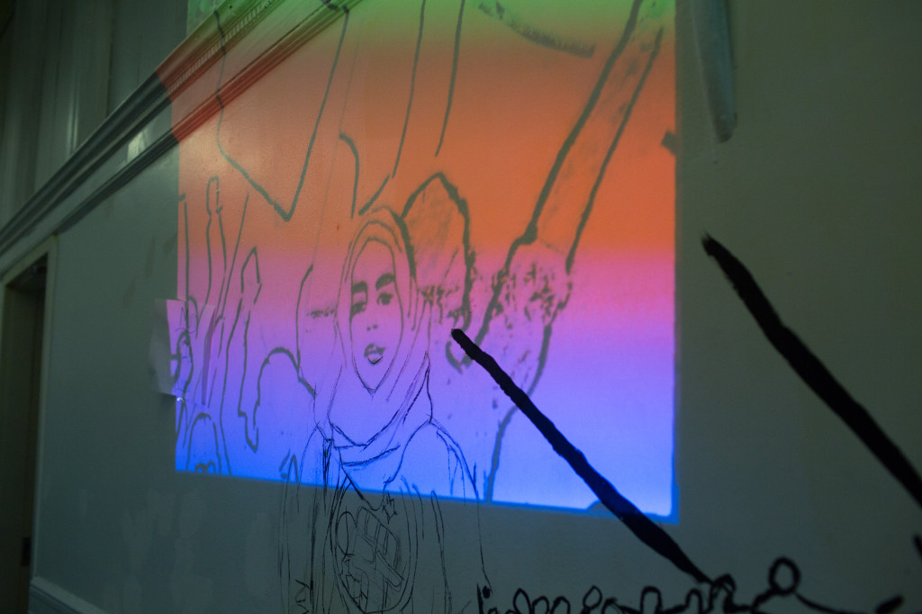 A photograph of the mural drawing is projected onto the wall for students to paint over. (CREDIT: Cassandra Giraldo)